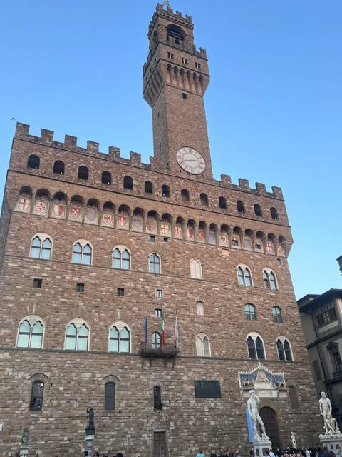 Stone facade of Palazzo Vecchio with large clock tower under clear sky