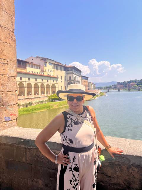 Woman in hat standing beside the Arno River with historic Florence buildings behind