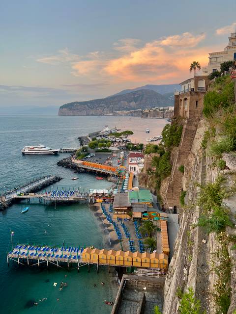 Cliff-top view of Sorrento marina with piers, umbrellas and boats on turquoise water