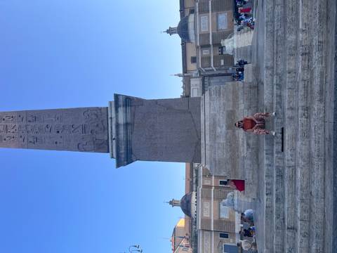 Woman seated on stone steps before towering ancient obelisk in open square