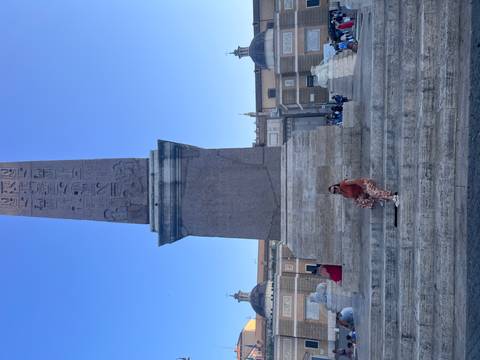 Single traveler seated on vast stone steps beneath tall obelisk and blue sky
