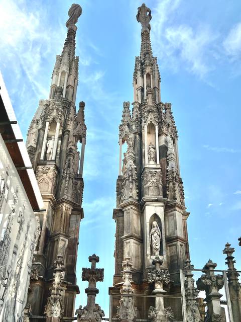 Two ornate marble spires of Milan Cathedral framed against bright blue sky