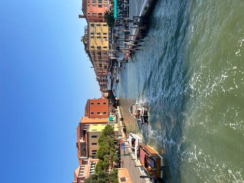 Canal scene with small motorboats, colorful houses and wake trails under blue sky