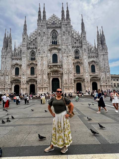 A smiling traveler poses in front of the ornate marble façade of Milan’s Duomo while other visitors wander the square.