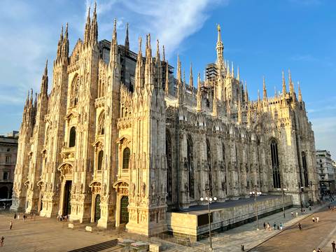Golden-hour light bathes the intricate spires and flying buttresses of Milan Cathedral against a clear blue sky.