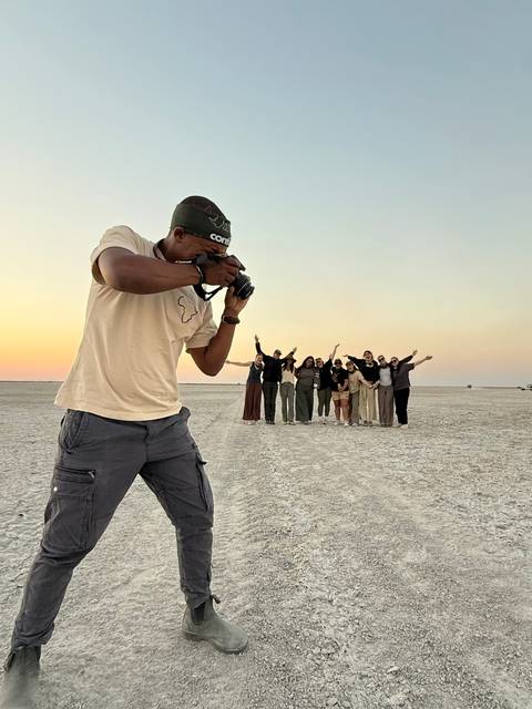 On a vast salt pan at twilight, a photographer captures a cheering tour group lined up in the distance.