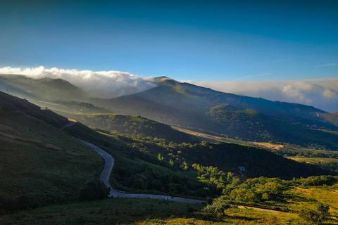 Morning light streams over layered mountain ridges shrouded in mist with a winding road below.