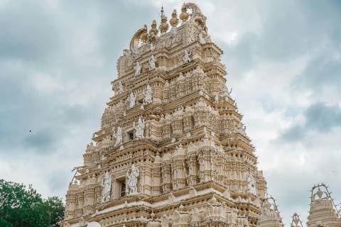 Elaborate white gopuram of a South Indian temple rises into a cloudy sky.