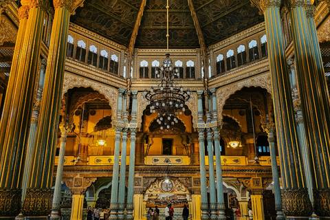 Opulent interior hall with ornate columns, chandeliers and arches illuminated by warm lighting.