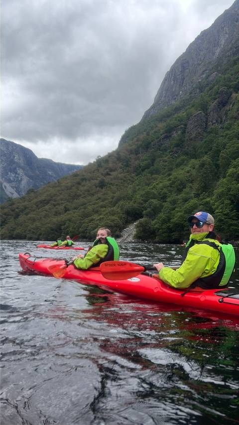 Kayakers in bright jackets paddling on a calm fjord surrounded by steep green mountains