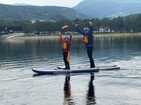 Adult and child triumphantly balancing on stand-up paddleboard on still lake surface