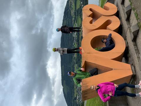 Family posing around giant orange VOSS sign with forested hills behind