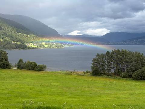 Scenic fjord landscape with vivid rainbow stretching over water between green valleys