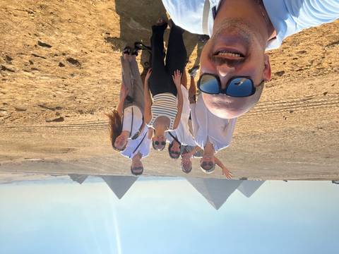 Group selfie on the desert plateau with three great pyramids rising behind them under bright sun.