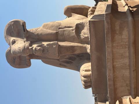 Close-up of a sandstone ram-headed sphinx statue under clear blue sky.