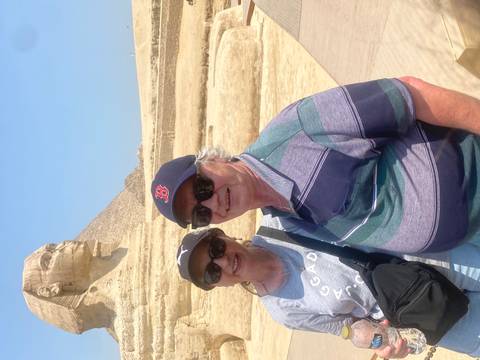 Older couple smiling in front of the Great Sphinx with part of a pyramid visible behind.