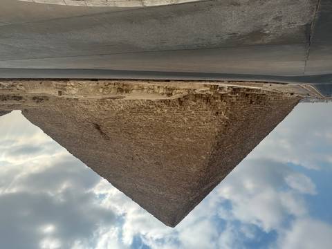 Wide view of a pyramid rising under partly cloudy skies with paved road in foreground.