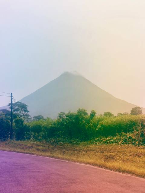 A mist-shrouded volcanic cone rises behind lush tropical vegetation