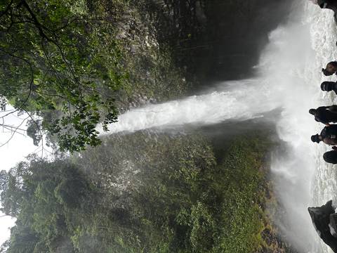 Tall jungle waterfall crashing into a pool where visitors gather at the base