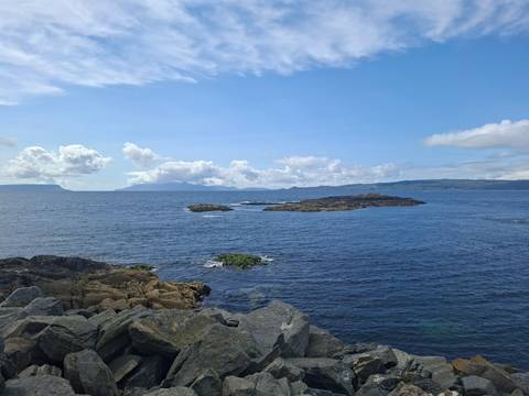 Bright blue sea with rocky islets and distant cloud-topped mountains