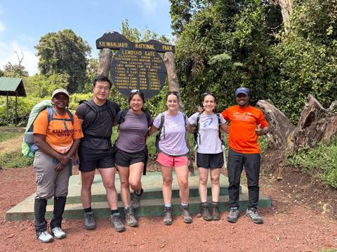 Trekking team posing at Lemosho Gate sign in Kilimanjaro National Park surrounded by forest greenery