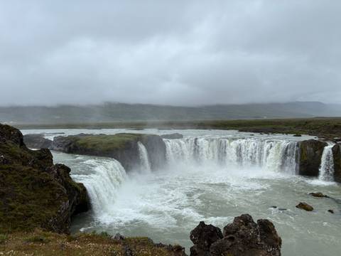 Powerful Godafoss waterfall cascading in multiple tiers amid mist under grey skies in Iceland