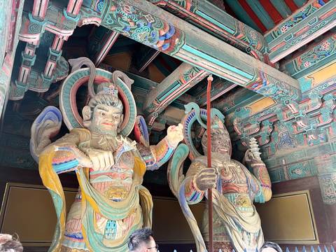 Vibrantly painted wooden guardian statues inside an intricately decorated Korean temple gate.