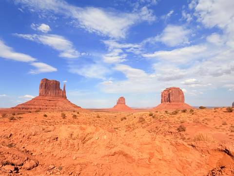 Iconic Mittens of Monument Valley rising from a red desert under bright blue sky