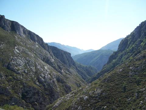 Wide rocky gorge framed by steep, rugged mountains under a clear blue sky.