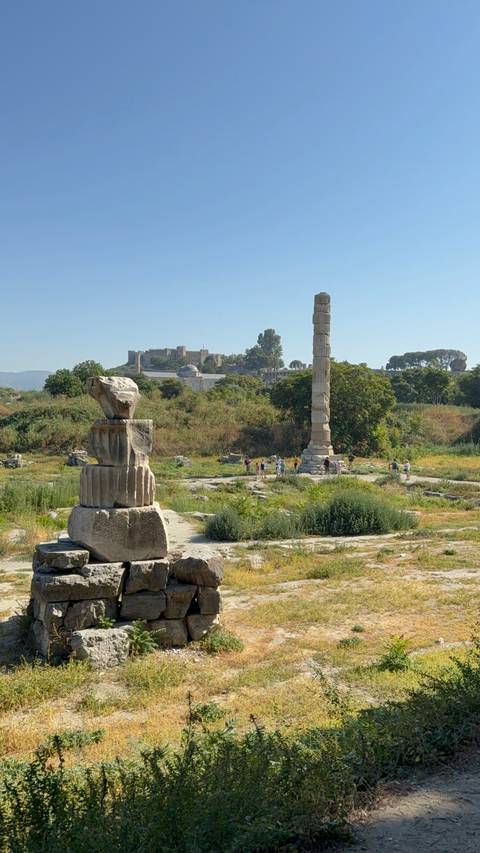 Ruins of the Temple of Artemis with a solitary column and distant fort overlook scattered visitors.