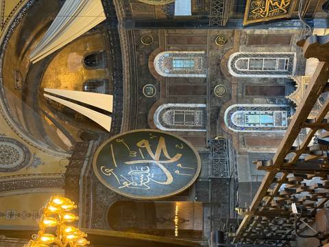 Interior gallery of Hagia Sophia showing giant Arabic calligraphy medallion and ornate mosaics.