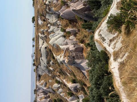 Eroded tuff hills and cave dwellings of Cappadocia rise among pale rock formations under clear sky.