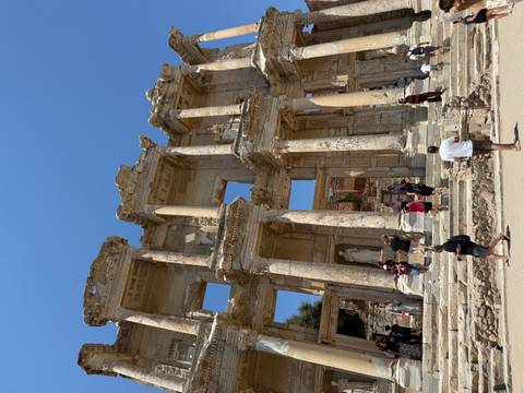 Tourists explore the marble facade of the Library of Celsus at Ephesus under bright blue sky.