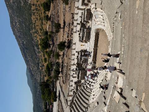 View down stone seating of the ancient Great Theatre of Ephesus with visitors scattered on the stage area.