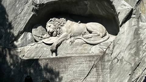 Carved Lion Monument of Lucerne lies in shadowed rock surrounded by engraved text.
