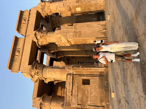 Couple poses before massive sandstone columns of Kom Ombo Temple in warm evening light.