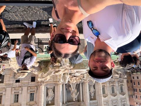 Couple takes a selfie at the Trevi Fountain surrounded by other tourists in Rome.