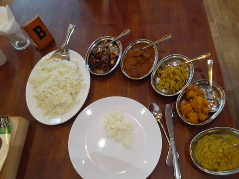 Sri Lankan meal with a plate of white rice and several small metal dishes filled with various curries laid out on a wooden table.