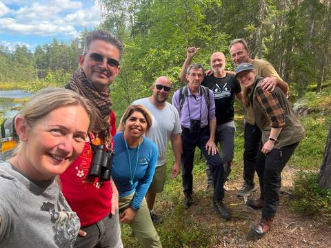 Smiling multi-national hiking group posing on forest trail near lake.