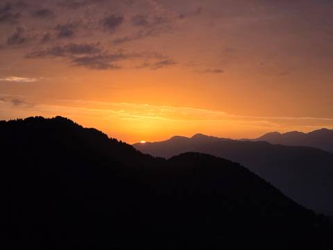 Fiery orange sunset dipping behind layered mountain silhouettes.
