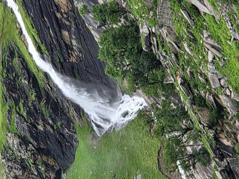 Tall waterfall cascading down rocky green mountainside.