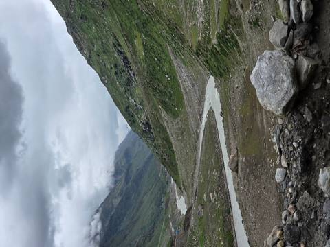 Winding river flowing through rocky alpine valley under cloudy skies.