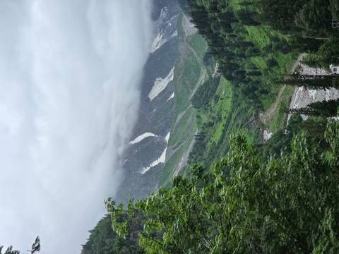 Lush green valley with patches of lingering snow beneath cloud-shrouded peaks.