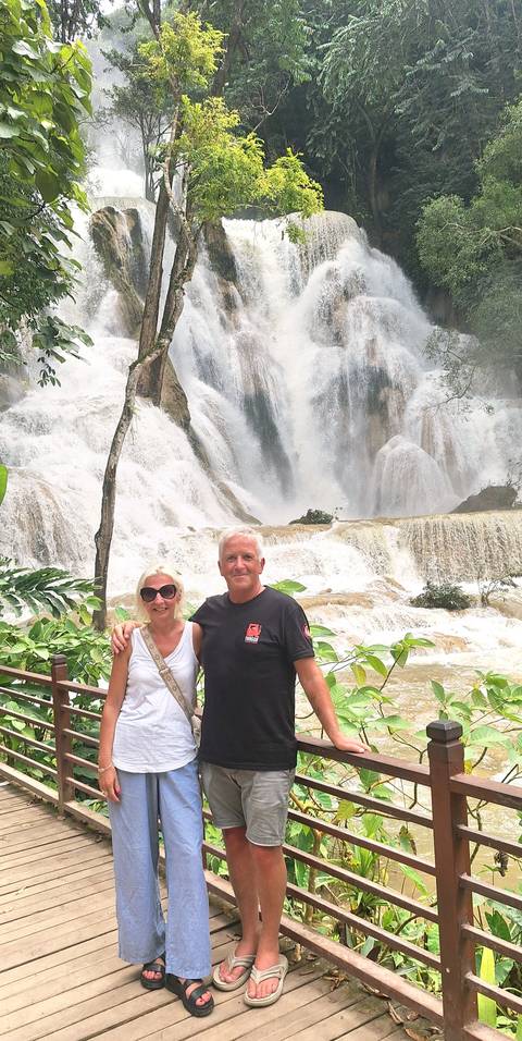 Couple smiling in front of powerful multi-tiered jungle waterfall.