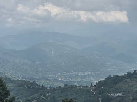 Hazy view across terraced hills and distant mountain ridges beneath a cloudy sky.