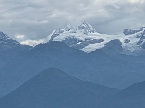 Snow-capped Himalayan peak rising above lower dark ridges on a cloudy day.