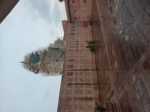 Courtyard of an Indian palace or mosque with a tall tower covered in scaffolding on a rainy day
