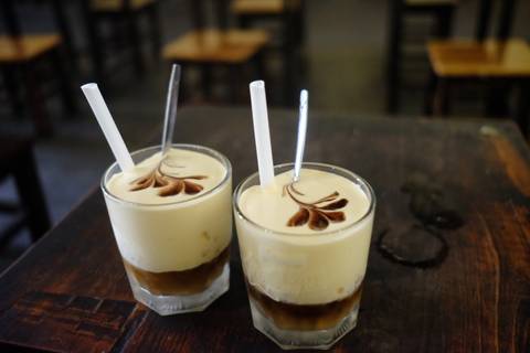 Close-up of two glasses of creamy Vietnamese egg coffee with chocolate art on top, sitting on a wooden table