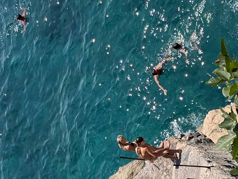 Travelers climbing and swimming from a rocky cliff into deep blue Mediterranean waters