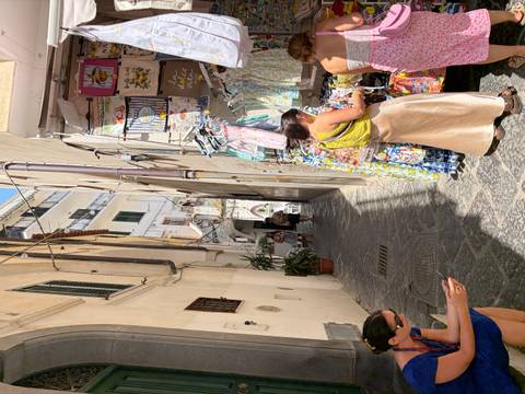 Narrow sunny alley in an Italian coastal town lined with souvenir stalls and shoppers
